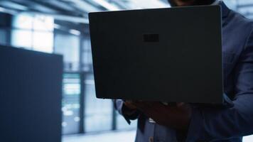Technician in server hub using laptop to patch network issues leading to slow data transfer rates. Close up of IT professional in data center fixing errors affecting supercomputers, camera B photo