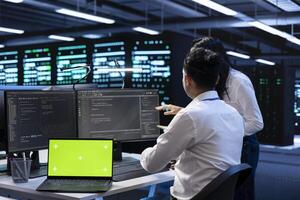 Team of technicians in data center using isolated screen laptop to find firewall misconfigurations affecting servers. IT staff members in server room checking systems bottlenecks using mockup device photo