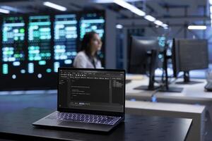 Focus on laptop in front of data center workers looking for firewall misconfigurations affecting servers. Close up on notebook used by system administrators in server room photo