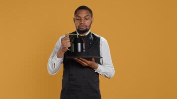 Restaurant staff serving clients with tea before their dinner order, bringing the teapot at the table. Waiter dressed in apron serves customers for satisfaction, service oriented industry. Camera B. photo
