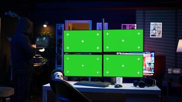 Hacker using isolated screen multi monitor PC setup, doing computer sabotage using ransomware. Cybercriminal walking with laptop, breaching firewalls in apartment with mockup displays, camera B photo