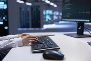 Close up shot of engineer in data center typing on keyboard, working on computer to do checkup on hardware mainframes. IT professional inputting data on PC in server farm photo