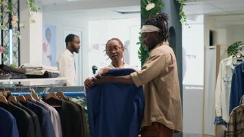 Man doing shopping in elegant fashion boutique, assisted by friendly shopkeeper with clothes. Customer receiving help from woman while trying on blazer from new collection stock photo