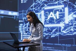 Engineer in high tech workspace managing call center tasks, speaking into headset while doing monitoring with laptop. AI company worker talking with clients through headphones mic photo