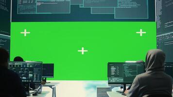Team of governmental hackers look at green screen in high tech agency office, working together on hacking database systems for cyberwarfare activity. Experts conducting illegal scams. Camera B. photo