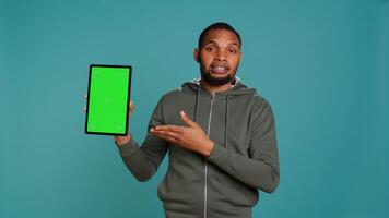 Happy influencer holding isolated screen tablet, doing recommendation, talking with audience. Cheerful person pointing towards chroma key digital device, isolated over studio background, camera B photo