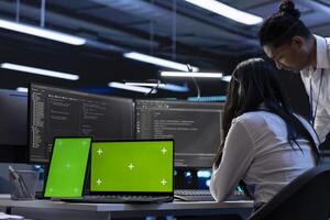 Engineers in data center using isolated screen laptop and tablet to find firewall misconfigurations affecting servers. Employees in server room checking systems bottlenecks using chroma key devices photo