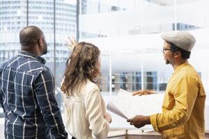Clients and real estate agent on an office tour reviewing workspace design and blueprints, negotiating leasing contract for urban property. Planning corporate relocation in a building. photo