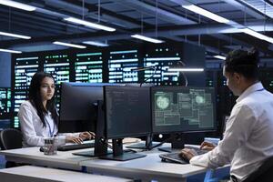 Programmers using computer in server room to support global connections using their hardware. IT professionals inspecting data center facility infrastructure supporting worldwide network photo