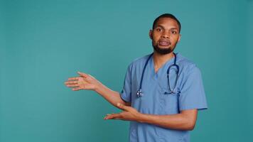 Portrait of african american nurse pointing hands towards empty space, doing advertising, talking with audience. Healthcare employee doing promotional ad, showing copy text, studio backdrop, camera B photo