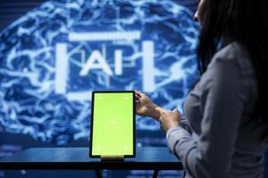 Startup coworkers brainstorming ways to use AI on chroma key tablet to improve data driven decisions. Technicians using mockup device to improve artificial intelligence tech photo