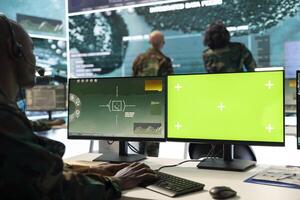Serviceman operates on surveillance footage and green screen display, monitoring battlefield satellite data on a computer in army base. Trooper IT engineer uses reconnaissance system. photo