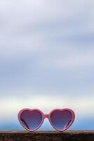 Heart-shaped sunglasses are placed on the balcony of the guest room against the blurred background of the sky. glasses are designed in pink heart to represent love and friendship between lovers. photo