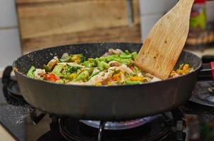 Colorful stir fry vegetables with chicken cooking in a pan on a gas stove in a home kitchen setting. photo