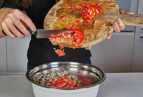 Close-up of hands throwing fresh tomatoes from a wooden cutting board into a pan with a knife in the kitchen photo