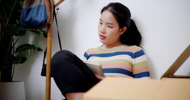 Handheld shot, Young Asian woman sitting on the floor and taking notes while thinking about house design in new house. Moving house and lifestyle concept. video