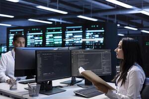 Team of engineers in data center checking emergency procedures documents to ensure system failure prevention. Colleagues in server farm workspace ensuring compliance with industry regulations photo