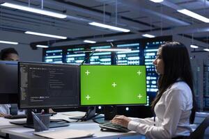 Coworkers in data center checking equipment performance on green screen computer after upgrading infrastructure. Engineers doing maintenance on supercomputers in servers room using mockup PC photo