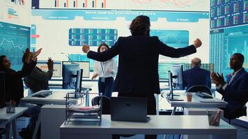 Business administrator celebrating expansion progress with his team, jumping around in the organizational coworking space. CEO is pleased about new fruitful investment and collaboration. Camera B. photo