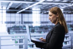 Admin implementing backup solutions in in data center service business to protect against equipment data loss using laptop. Expert resolving technical malfunctions affecting rackmounts using notebook photo