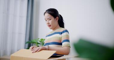 Handheld selective focus shot, Young Asian woman pack belongings into cardboard boxes and wrapping with duct tape in preparation for moving into new house. Moving house and lifestyle concept. video