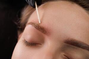 After the first permanent makeup procedure, anesthesia is applied to the eyebrow using a cotton swab. Permanent eyebrow makeup PMU for brunettes photo