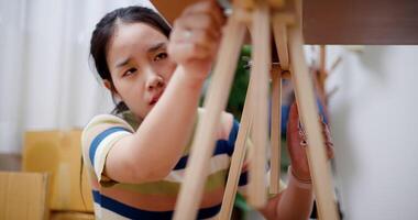 Handheld selective focus shot, Young Asian woman sitting on the floor and assembling wooden furniture in a new house. Moving house and lifestyle concept. video