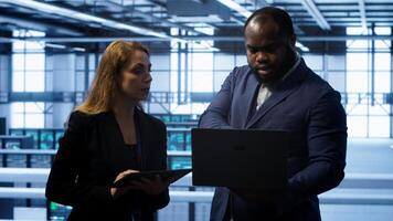 Team of IT specialists managing data center with advanced technology using devices. Coworkers in server room optimizing data center hardware equipment with laptop and tablet, camera A photo