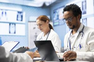 Diverse team of medics examining x ray results and healthcare data in a cabinet meeting, consulting the colleagues before putting a diagnostic. Physicians working together for healthcare recovery. photo