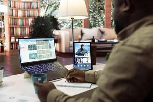 Entrepreneur transmitting financial data reports and discussing resources allocations with shareholders on a videocall from his home desk. Businessman meets with investors online. photo