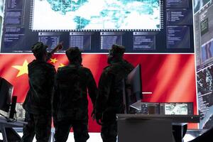 Military intelligence officers from China analyze surveillance data on a big screen in a chinese command center. Soldiers discussing warfare tactics for a terrorist attack, high tech cyber network. photo