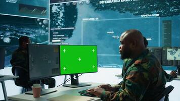 Military expert handles satellite cctv data next to mockup screen, working in a base of operations with high tech gear to support important defense missions. Coordinates strategic tactics. Camera B. photo