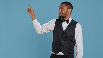 Doorkeeper bellhop pointing at something to left or right sides, indicating the direction for multiple amenities at the five star resort. Bellboy staff wearing a tuxedo uniform at his job. Camera B. photo