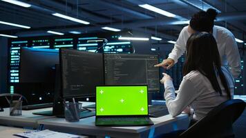 Engineer in high tech data center managing and maintaining databases using mockup devices, ensuring data integrity. Indian employees updating server room supercomputers with chroma key laptop photo