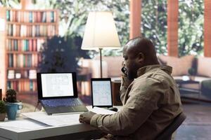 Business owner discussing new office space layout with contractors via phone call, finding architectural interior design inspiration from blueprints and sketches. Planning a workspace relocation. photo