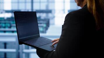 Technician doing checkup, inputting data on laptop of needed server hub fixes. Close up of employee working in data center housing advanced storage infrastructure supporting IT workloads, camera A photo