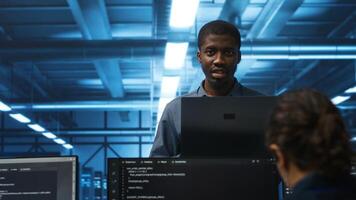 Portrait of happy manager supervising server rows in computer network security data center. Smiling african american supervisor and employees overseeing supercomputers in server hub photo