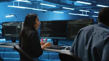 Team of IT support experts working together, supervising server rows in computer network security data center. Woman next to colleagues talking in headphones mic while overseeing supercomputers photo
