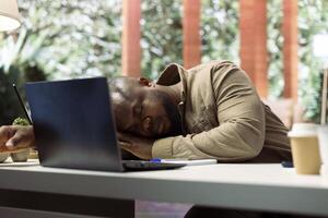 Entrepreneur sleeping on his home office desk after stressful analysis for the online business he is running. Tired fatigued businessman getting some rest with a nap, burnout. photo