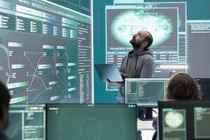 Hacker specialist working on governmental cyber surveillance in agency center, examining stolen information on a big screen during hybrid war. IT expert works on intelligence espionage. photo