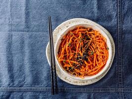 Spicy sesame carrot noodles salad ready-to-eat overhead. Vegetable carrot spaghetti with black sesame and thyme. Clean eating, raw vegetarian food concept. Flat lay or top view. Copy space for text. photo