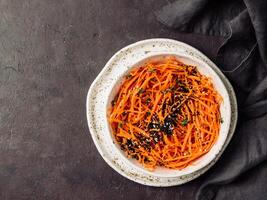 Spicy sesame carrot noodles salad ready-to-eat overhead. Vegetable carrot spaghetti with black sesame and thyme. Clean eating, raw vegetarian food concept. Flat lay or top view. Copy space for text. photo