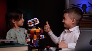 Two kids showing thumbs up while building robot from plastic bricks photo