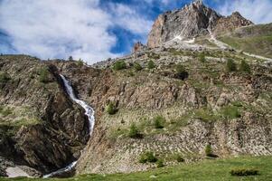 a waterfall in the mountains with a mountain in the background photo