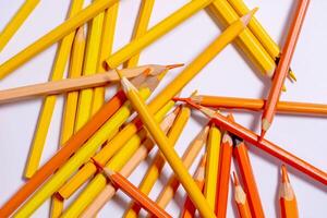 scattering of chaotically scattered yellow, beige and orange colored pencils on a white background, top view photo