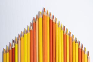 yellow and orange pencils stacked together with leads upwards in the form of a triangle with a top in the center on a white background photo