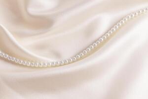 Chic cream-colored satin with a string of pearl beads among the soft waves of fabric. Wedding holiday backdrop for design. A copy space photo