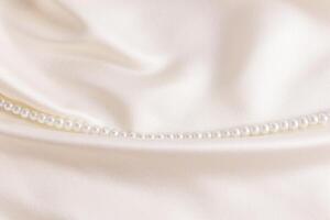 Stylish modern wedding background chic cream-colored satin with a string of white pearl beads from left to right on a fold of fabric. A copy space. photo