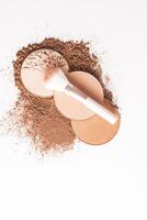 Three round blocks of compact powder in different tones, a makeup brush lies on them. top view. white background. a layout product. vertical top view. photo