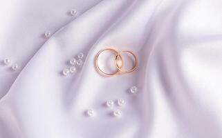 Chic wedding background with wedding gold rings lying on a wave of white satin fabric and pearls. The concept of the wedding. postcard. top view. photo